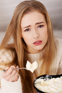 Sad, worried beautiful woman eating ice cream. Indoor background